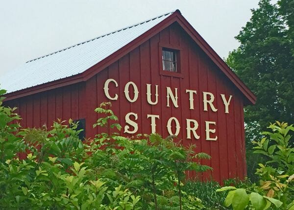 16x20 Barn (post and beam livestock shelter) that has been painted red with a wooden Country Store sign installed on it. 