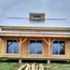 20-by-30-foot timber frame cabin with open porch with overhang roof, cupola, three sliding glass doors, and lumber on grass.