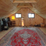 Interior of cabin loft with shiplap pine interior sheathing, a large red Oriental area rug, two windows, and stereo equipment.