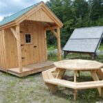 8x12 Nook post and beam cabin sitting next to an octagon picnic table and solar shed