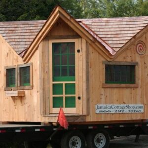 This small cottage is shown with a red cedar shingle roof, glass roundel, and a custom window and door layout with  aflower box.