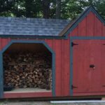 8x14 Vermont Gem firewood storage shed painted red with blue trim and an asphalt shingle roof