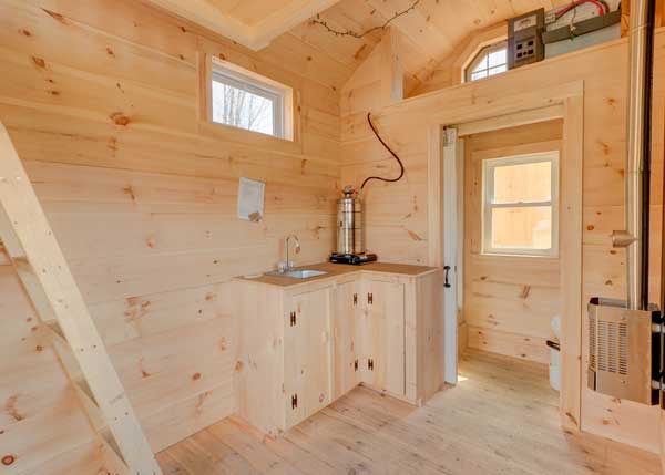 Tiny house interior with a storage loft, kitchenette, and partitioned off bathroom.