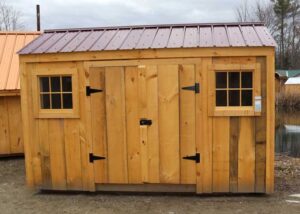 This small post and beam storage shed has two barn sash windows, a double door, and a red roof. 
