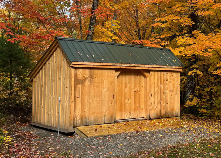 16 foot wide shed with three sliding barn doors, a ramp, and a green metal roof sits among colorful autumn foliage.