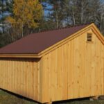 Saltbox storage shed with a brown metal roof and wood louvered vent.