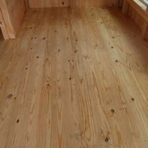 Pine tongue and groove flooring, also called wood floor decking in a four-season Florida room of a rustic tiny house cabin.