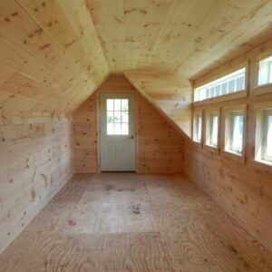 Interior of post and beam cabin with shiplap pine ceiling and wall sheathing, plywood floors, and dormer with row of windows.