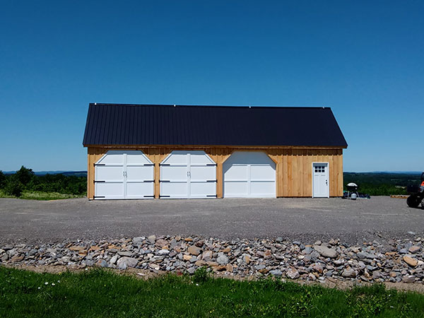This post and beam equipment shed is shown with some modifications made by the client. They ordered custom doors for the four openings. They needed to order extra siding to enclose the fourth bay that has the single door.