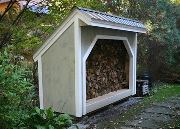 Custom built firewood storage shed painted green with a matte black metal roof.