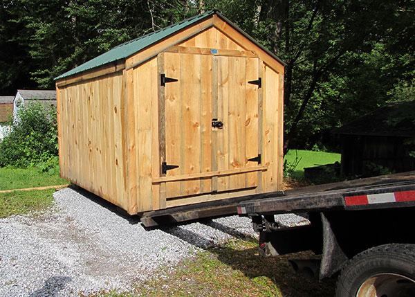 A fully assembled storage shed being lowered onto a gravel foundation.