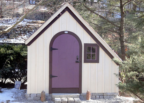 6x10 Hardware Shed painted white with purple trim and door on a fancy stone foundation