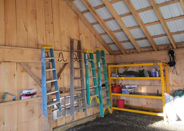 An organized post and beam garage showing a storage shelf and hanging latter